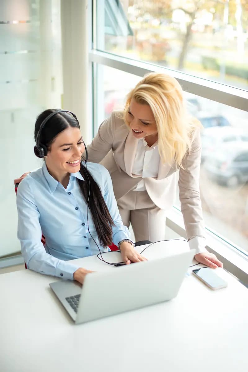 A manager helping a customer-support specialist at a laptop